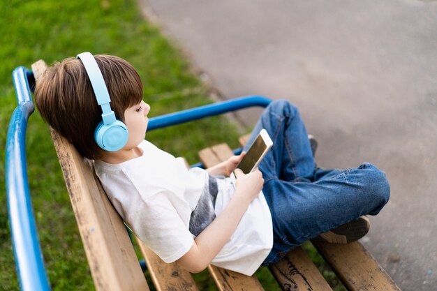 Un garçon dans la rue est assis sur un banc avec des écouteurs et un téléphone