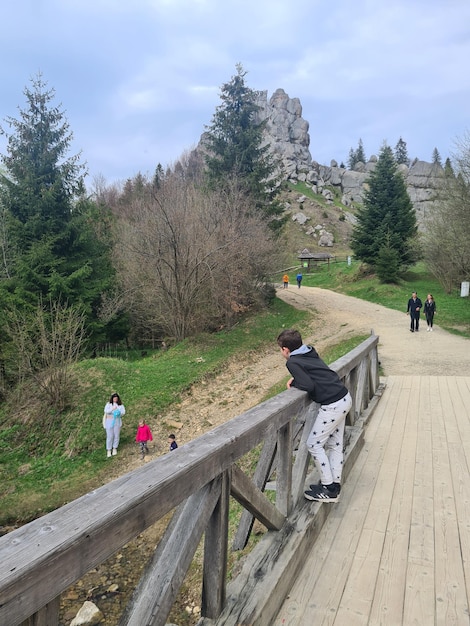 Un garçon dans un sweat à capuche noir se tient sur une clôture en bois devant un château.