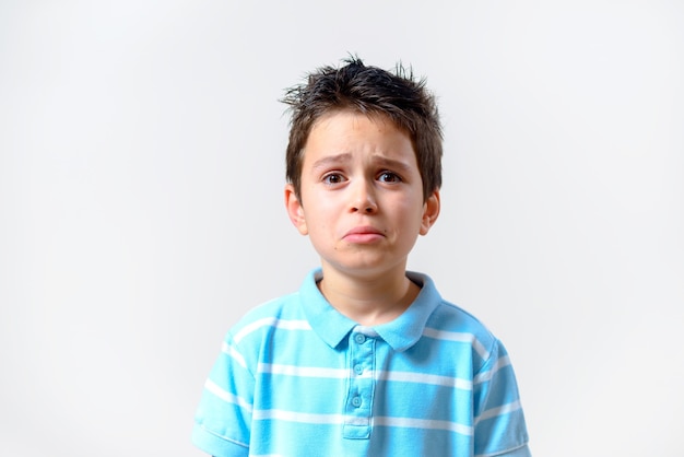 Le garçon dans un T-shirt bleu avec une expression mécontente regarde la caméra.