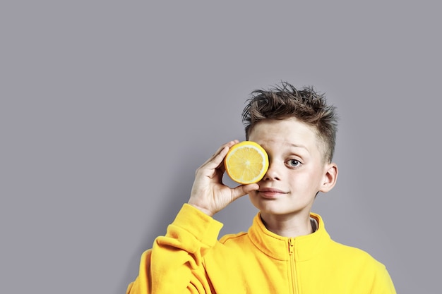 Un garçon dans une veste jaune vif avec un citron à la main sur un fond bleu