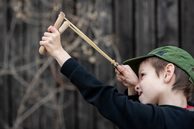 Un garçon dans une veste noire avec une capuche et une casquette tire d'un arrière-plan flou de fronde