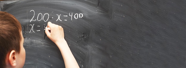 Garçon debout devant le tableau noir de l'école et écrivant