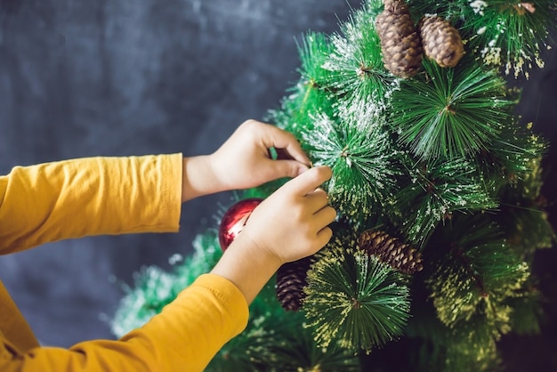 Garçon décorant le sapin de Noël avec des boules et des pommes de pin