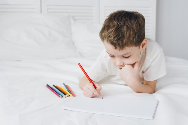 Garçon dessine avec des crayons colorés assis sur le lit