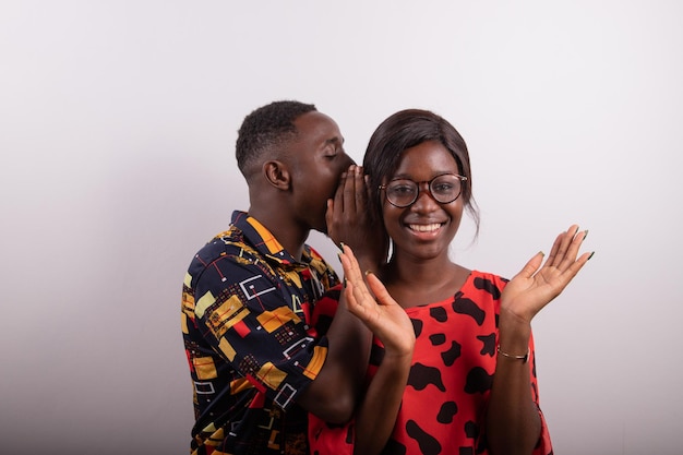 Un garçon dit quelque chose à une fille en lui parlant à l'oreille, elle est surprise Concept de surprise studio photo