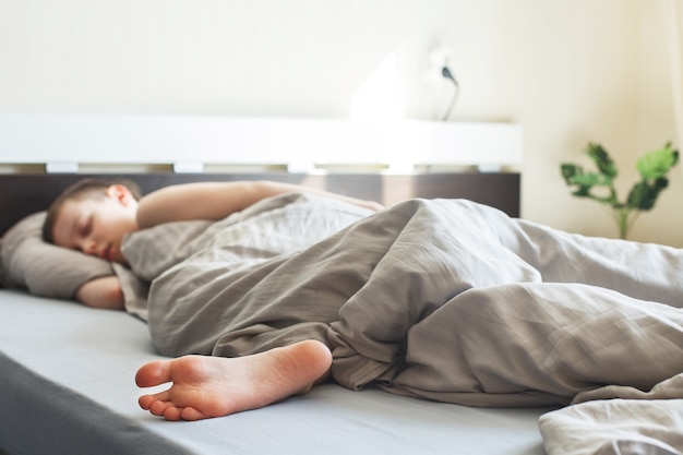 Le garçon dort dans le lit sous une couverture