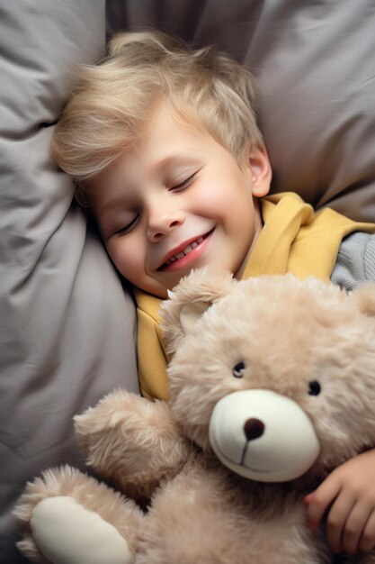 Le garçon dort doucement dans le lit avec un ours en jouet dans ses bras sous la couverture.