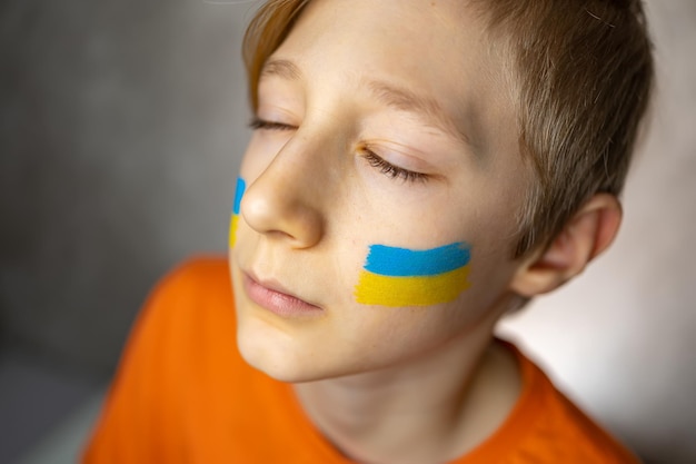 Le garçon avec le drapeau peint de l'Ukraine ferma les yeux et leva la tête vers le haut