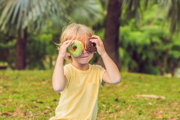 Garçon drôle avec beignet. l'enfant s'amuse avec le beignet. Nourriture savoureuse pour les enfants. Bon moment en plein air avec des aliments sucrés.