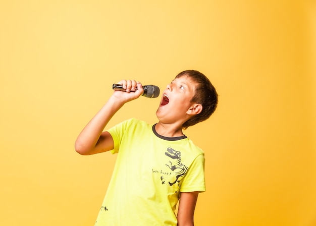 Garçon drôle chantant avec le microphone sur le fond jaune