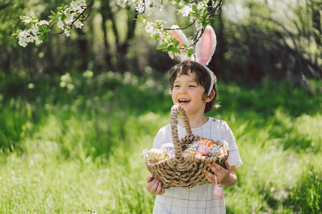 Garçon drôle avec panier d'oeufs et oreilles de lapin sur la chasse aux oeufs de pâques dans le jardin de printemps ensoleillé