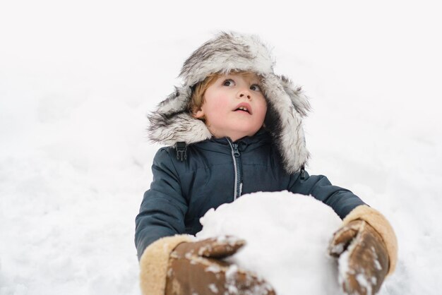 Garçon drôle posant sur l'enfant de temps d'hiver jouant avec la boule de neige