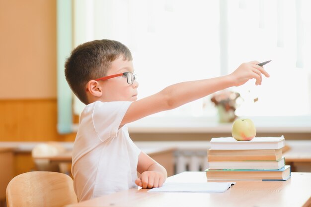 Garçon de l'école primaire au bureau de la classe essayant de trouver de nouvelles idées pour le travail scolaire.