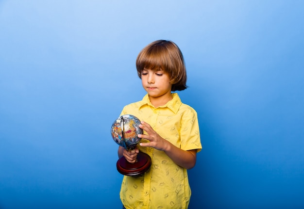 Garçon écolier 7 ans écolier avec un globe souvenir dans ses mains souriant sur fond bleu