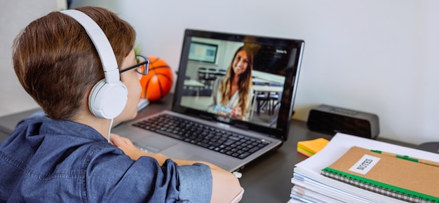 Un garçon avec des écouteurs qui reçoit des cours à la maison avec un ordinateur portable de son