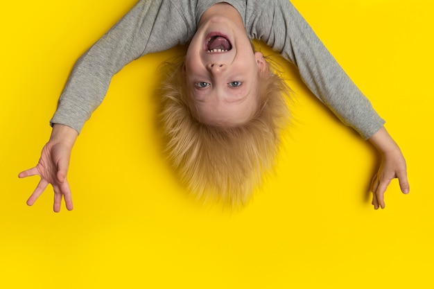 Garçon effrayé avec de longs cheveux blonds pend à l'envers et crie.