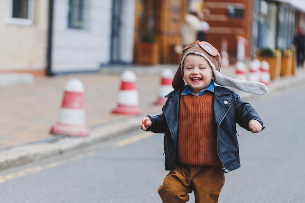 Garçon élégant de 3 ans dans une veste en cuir et un pantalon marron se promène dans la rue Enfant moderne Mode enfantine Enfant heureux
