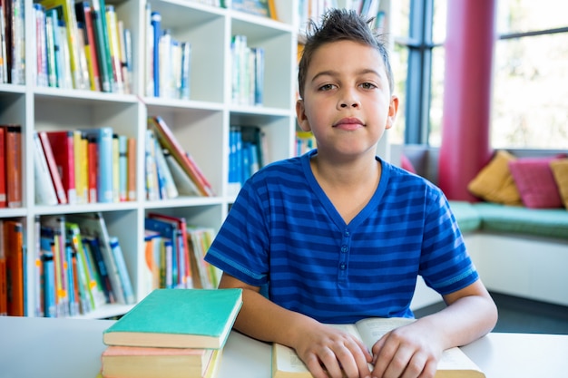 Photo garçon élémentaire, lecture de livre dans la bibliothèque de l'école