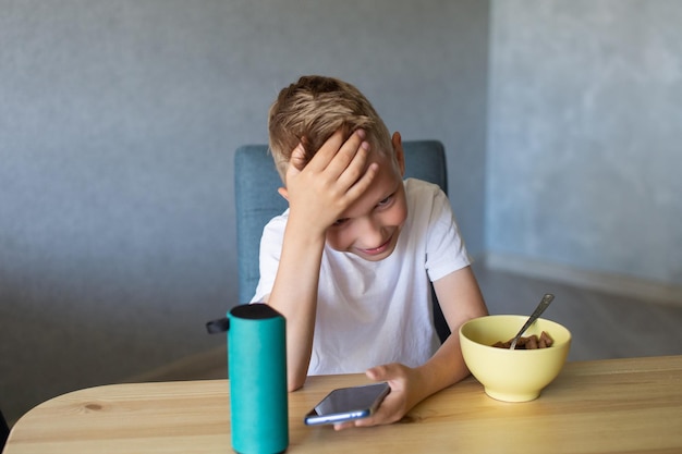 Un garçon émotif dans un t-shirt blanc connecte le haut-parleur au téléphone et rit