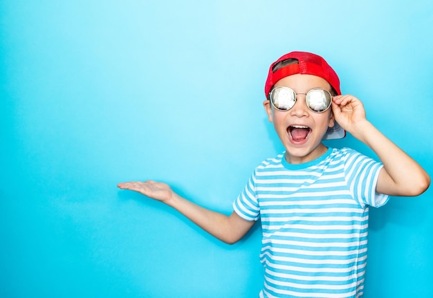 Garçon émotionnel à lunettes de soleil avec une casquette de baseball sur la tête sur un fond bleu isolé