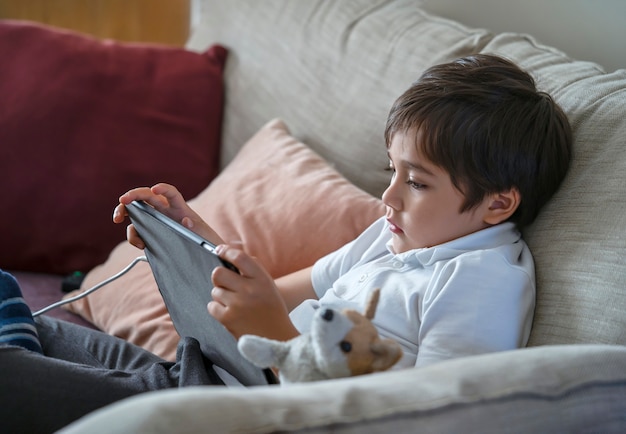 Garçon enfant assis sur le canapé à regarder des dessins animés sur téléphone mobile, enfant de l'école à l'aide de téléphones portables, cours d'apprentissage sur internet, enseignement à domicile, concept d'éducation en ligne à distance