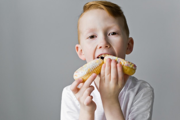 Garçon enfant avec des beignets blancs sur fond gris.