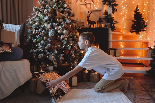 Garçon enfant décorant l'arbre de Noël à la maison. Une famille avec des enfants célèbre les vacances d'hiver. Les enfants décorent le salon et la cheminée pour Noël.