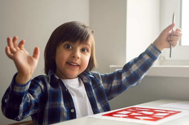 Garçon enfant dessine sur papier avec une règle sur une table assise près de la fenêtre