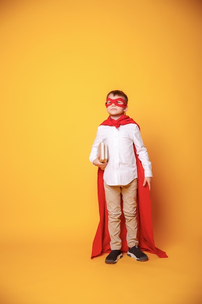 Garçon enfant écolier avec lunettes hol livre dans ses mains dans un costume de super héros sur fond jaune