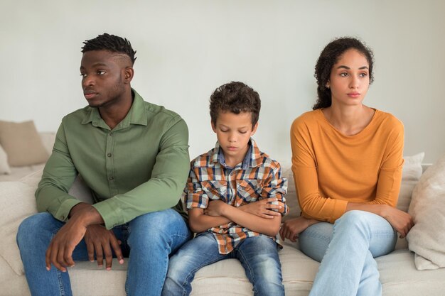 Photo garçon enfant malheureux assis entre divers parents boudant à la maison