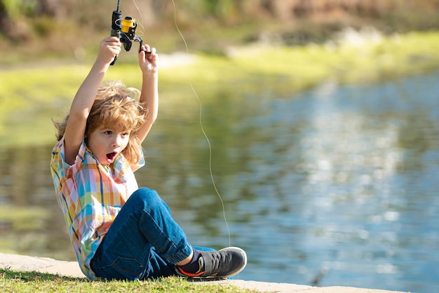 Un garçon enfant pêcheur se tient dans la rivière avec une canne à pêche et attrape du poisson