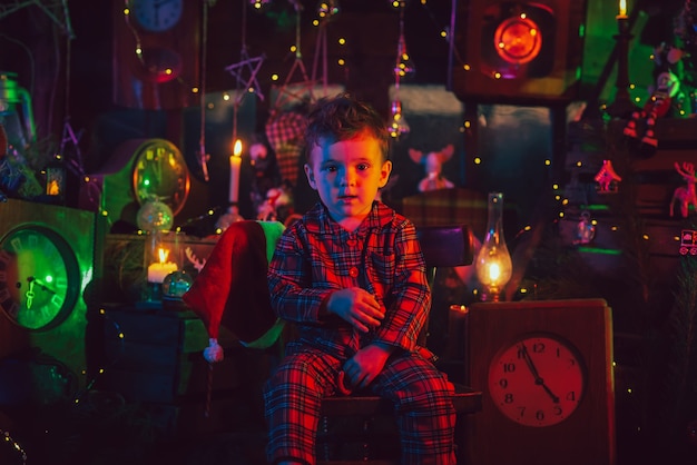 Un garçon-enfant, en pyjama de Noël à carreaux dans une ambiance festive de nouvel an. Photo sur une carte postale avec une lumière colorée.