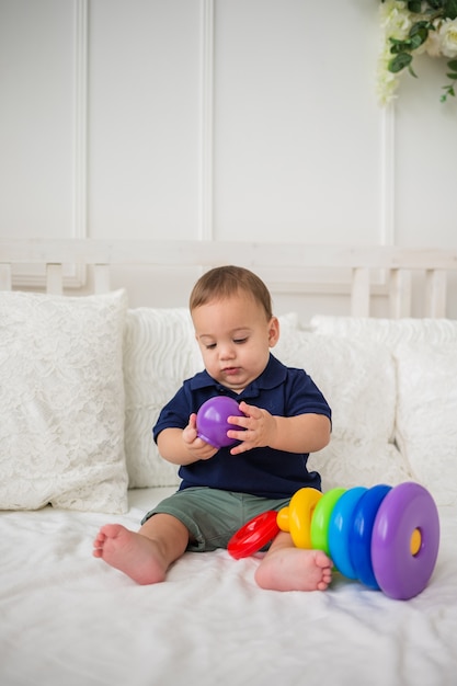 Garçon enfant sérieux recueille jouet pyramide sur lit blanc