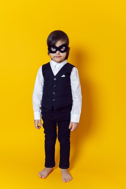 Garçon enfant super héros dans un costume et un masque noir sur un mur jaune pieds nus