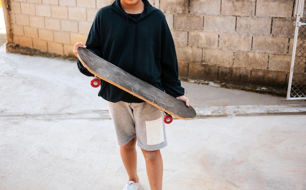 Garçon enfant tenant une planche à roulettes contre le mur de blocs de ciment