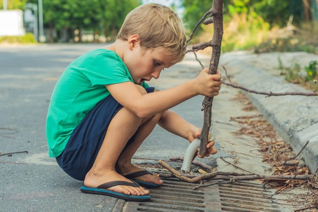 Garçon espiègle blond farceur avec des taches de rousseur jouant pousse le bâton vers le bas de la route drain émotions artistiques expression faciale gesticulant Relation familiale micro moments de l'enfance humanité société