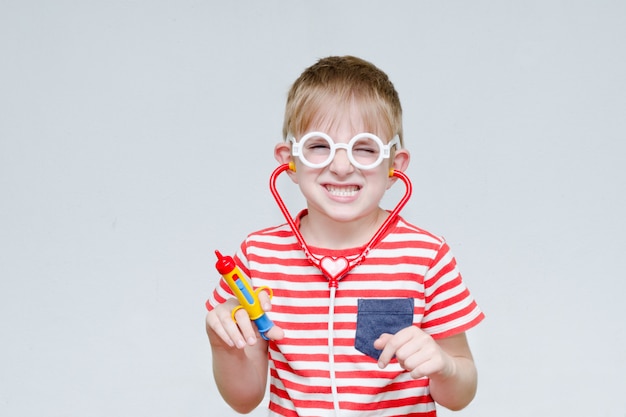 Garçon espiègle jouant au docteur. Seringue jouet, lunettes et phonendoscope. Portrait