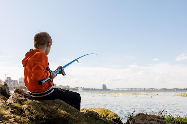 Le garçon essaie de tirer le poisson hors de la rivière à l'aide d'une canne à pêche sa canne à pêche se plie du poisson