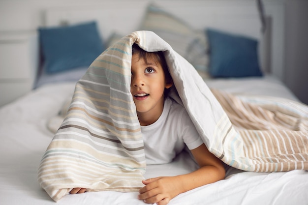 Un garçon est allongé dans son lit sous une couverture rayée et ne veut pas dormir, insomnie et amusement