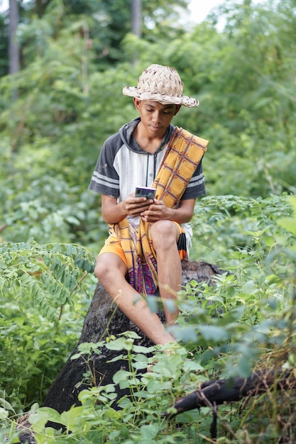 Un garçon est assis sur une bûche dans les bois et regarde son téléphone.