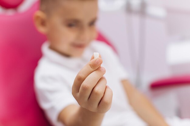 Le garçon est assis dans un fauteuil dentaire lors d'une visite chez le dentiste et montre une dent perdue