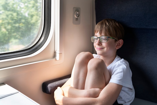 Le garçon est assis dans la voiture du compartiment et serre ses genoux. Voyage en train.