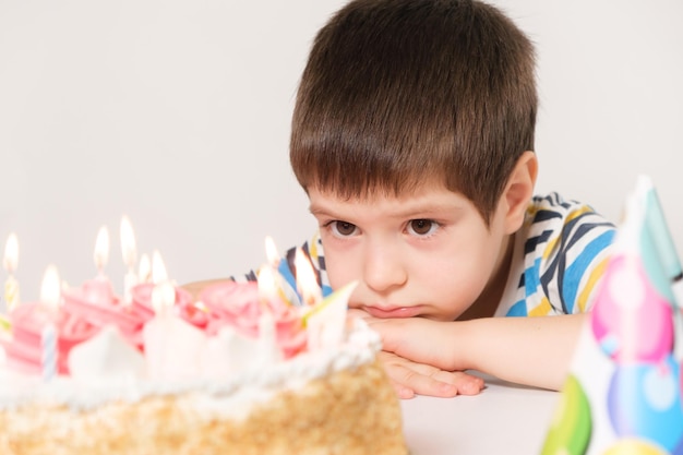 Un garçon est assis devant un gâteau avec des bougies et fait un vœu