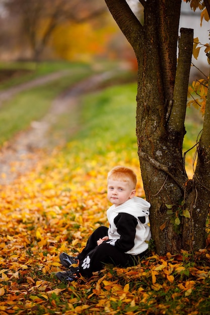 Un garçon est assis sous un arbre à l'automne et regarde le ciel comme un oiseau Beaux vêtements pour enfants