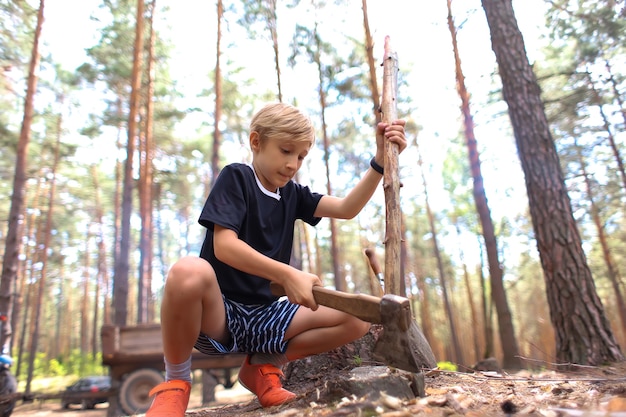 Le garçon est dans une forêt de pins et coupe du bois pour faire un feu