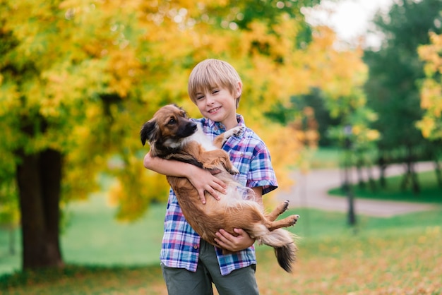 Garçon étreignant un chien et plyaing avec dans le parc de la ville d'automne