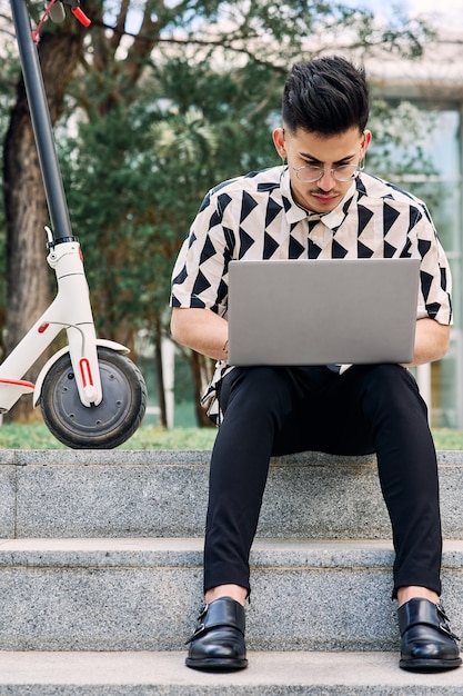 Photo garçon étudiant dans un parc avec un ordinateur portable et un scooter