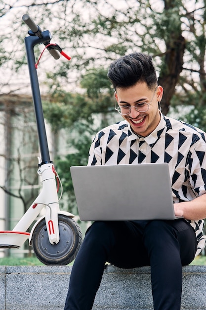 Garçon étudiant dans un parc avec un ordinateur portable et un scooter