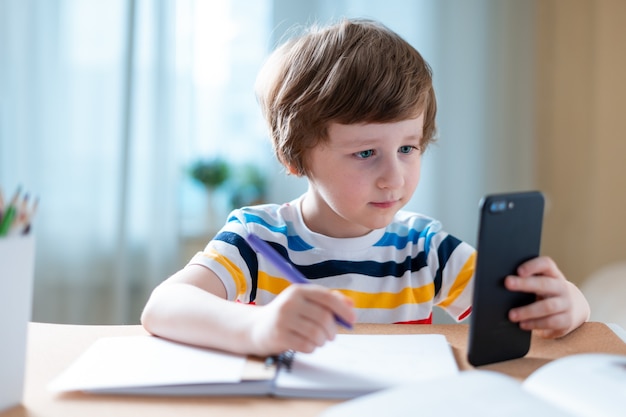 Garçon étudiant à la maison avec smartphone et faire ses devoirs scolaires.