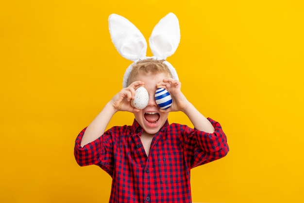 Garçon excité dans des oreilles de lapin sur la tête et des oeufs de Pâques sur les yeux sur jaune